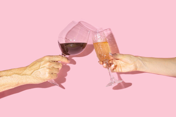 Celebrity concept. Two hands, man one holding glass of vine and girl hand holding antique crystal glasses with lovely drinks in it against baby pink background - Photo, Image