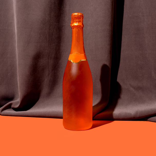 Een roos kleur bootle van champagne tegen stemmige rijke en donkere fluwelen achtergrond, plons van terracotta balg - Foto, afbeelding