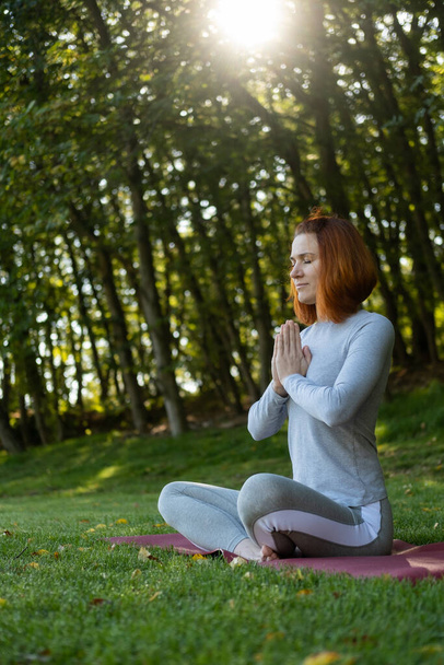 Millennial sottile zenzero donna facendo yoga all'aperto sulla natura in città in autunno giornata di sole all'alba. - Foto, immagini