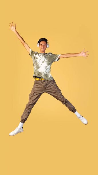 Portrait of young handsome boy, student in casual clothes jumping isolated on yellow studio backgroud. Human emotions concept. - Фото, зображення