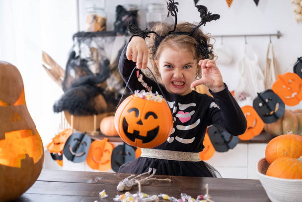 Cadı kostümü içinde küçük şirin bir kız elinde şekerle balkabağı Jack 'i tutuyor mutfakta eğleniyor, Cadılar Bayramı' nı kutluyor.. - Fotoğraf, Görsel