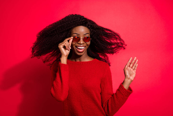 Photo of young black girl happy positive smile hand touch glasses fly air hair isolated over red color background - Фото, зображення
