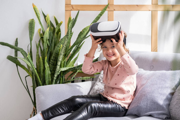Cute little girl in virtual reality glasses at home. happy kid using VR headset. - Photo, image