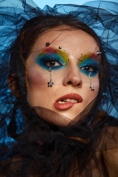 Fashion creative make up. Beautiful portrait of young woman with clean fresh skin and bright make up with rhinestones on her face posing on a bright blue background - Foto, Imagen