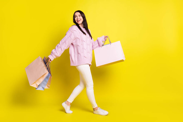 Full body profile photo of impressed millennial lady hold bags go look empty space wear sweater pants isolated on yellow background - Φωτογραφία, εικόνα