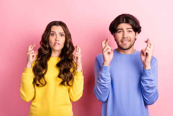 Photo of young couple worried nervous crossed fingers wish luck success isolated over pink color background - Фото, изображение