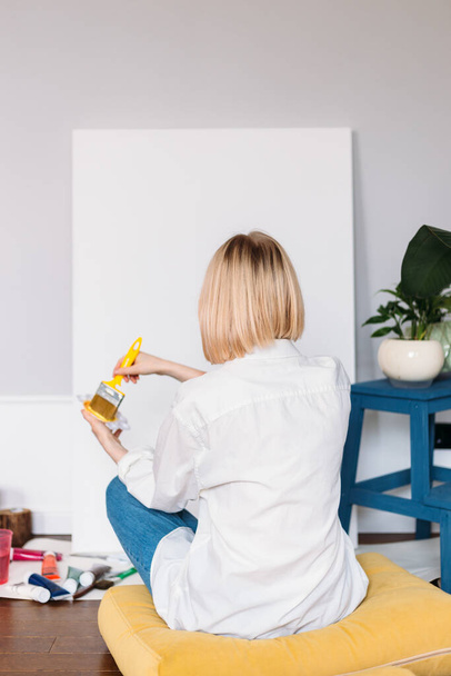 Νεαρή γυναίκα καλλιτέχνης ζωγραφίζει στο σπίτι σε ένα δημιουργικό σκηνικό στούντιο.  - Φωτογραφία, εικόνα