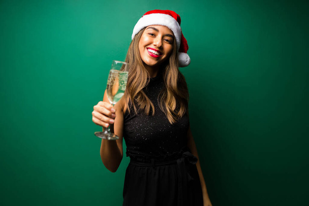 Вітаю! Чудова жінка в капелюсі Санти робить тост з шампанським під час різдвяної вечірки
 - Фото, зображення