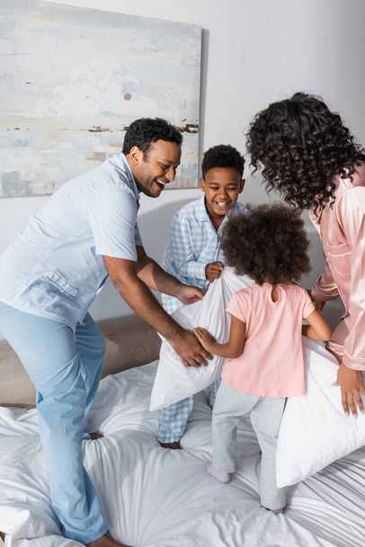joyful african american parents and kids holding pillows while having fun on bed - Fotó, kép