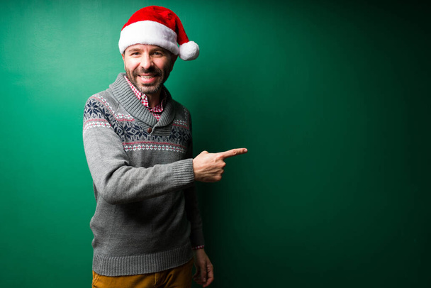 Jovem alegre com um chapéu de Natal apontando ao lado do espaço de cópia na frente de um fundo verde - Foto, Imagem
