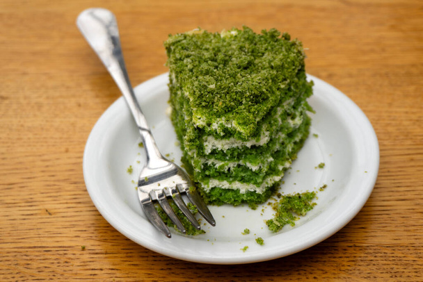 Green pistachio pie with white cream bitten on a saucer in a cafe with a dirty fork - Фото, изображение