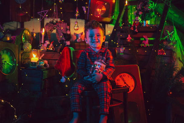 クリスマスのパジャマと帽子の幸せな子供の男の子、クリスマスの魔法の装飾のサンタヘルパー. - 写真・画像