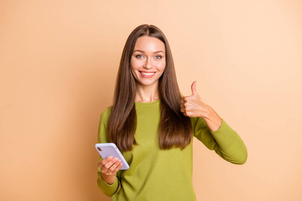 Porträt von attraktiven fröhlichen Mädchen mit Gerät, das Daumen nach oben Werbung isoliert über beige Pastellfarbe Hintergrund - Foto, Bild