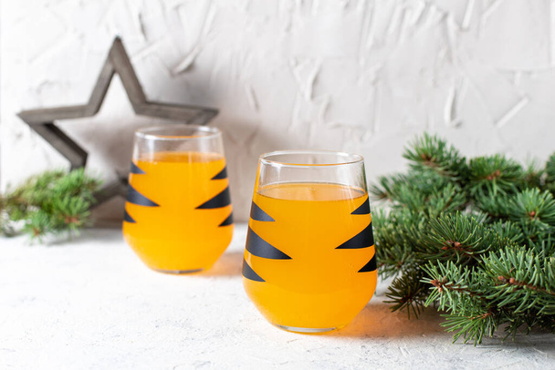 cóctel de mandarina naranja en vaso con rayas negras. Bebida de bienvenida navideña. Concepto para niños año nuevo con ramas de árboles - Foto, Imagen