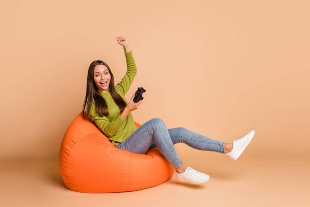 Portrait of lovely cheerful girl sitting on bag chair playing video game having fun isolated over beige pastel color background - Foto, Imagem