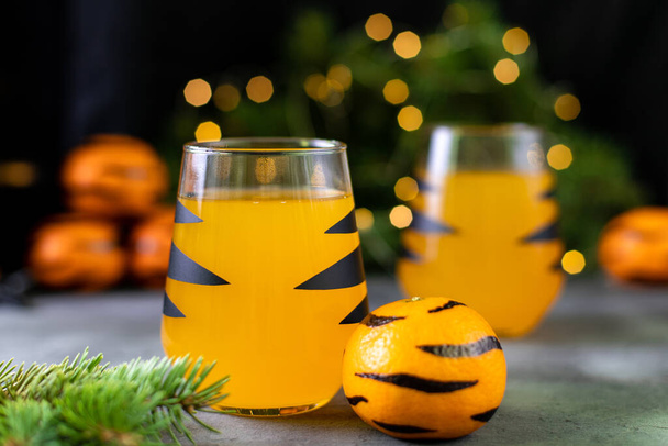 oranje mandarijn cocktail in glas met zwarte strepen. Kerstvakantie welkomstdrankje. Concept voor kinderen Nieuwjaar met boomtakken en gestreepte mandarijnen met bokeh - Foto, afbeelding