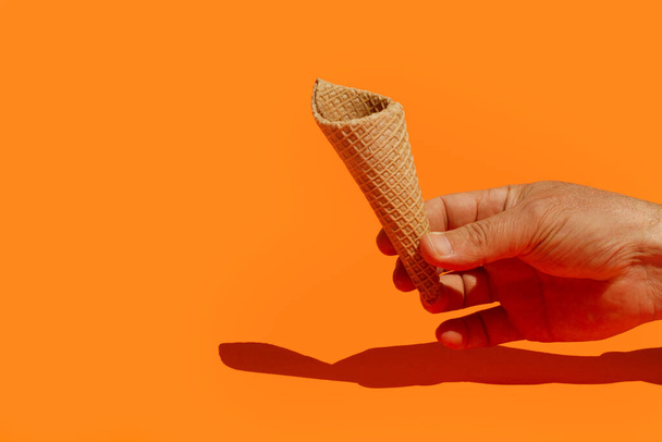 Mão de homem segurando um cone de bolacha em um fundo laranja - Foto, Imagem