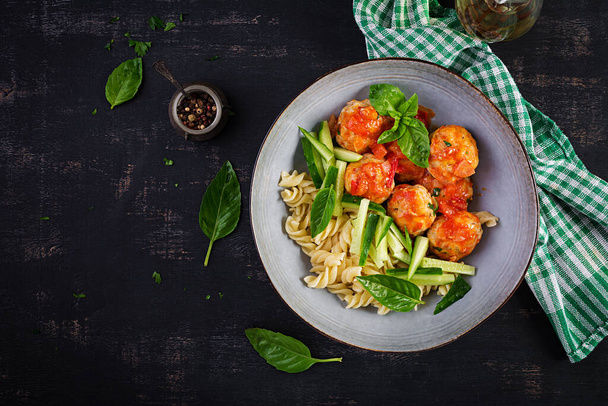 Italiaanse pasta. Fusilli met gehaktballen, komkommer en basilicum op donkere achtergrond. Uit eten. Slow food concept. Bovenaanzicht, vlak lay - Foto, afbeelding