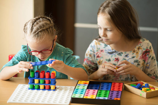 Una ragazza con la sindrome di Down è impegnata in matematica elementare con la sorella maggiore, divertendosi a giocare - Foto, immagini