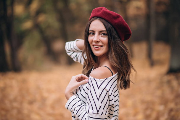 Portrét brunetky na podzim v parku. Francouzský styl. Žena v baretu a pruhované blůze - Fotografie, Obrázek