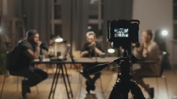 Rastreamento tiro de câmera de vídeo filmando três pessoas sentadas à mesa na sala de estar e ter uma conversa durante a gravação de podcast - Filmagem, Vídeo