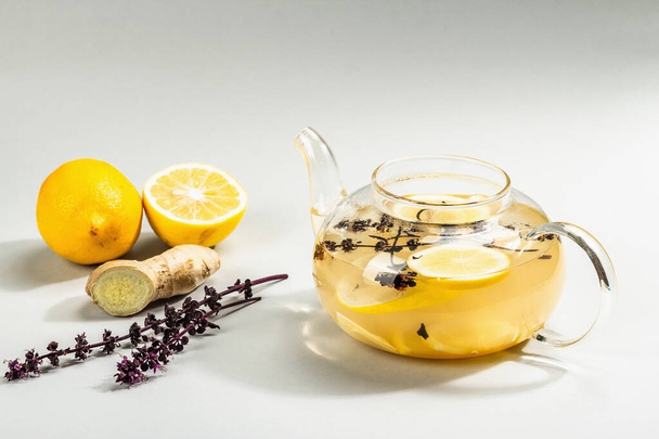 Hot ginger tea with lemon and honey in a glass cup on light grey background. Alternative medicine, natural home remedy for cold and flu, modern hard light, dark shadow, copy space - Фото, изображение