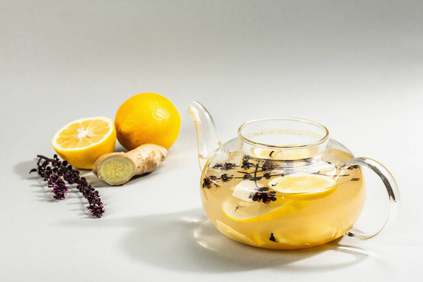 Hot ginger tea with lemon and honey in a glass cup on light grey background. Alternative medicine, natural home remedy for cold and flu, modern hard light, dark shadow, copy space - Photo, Image