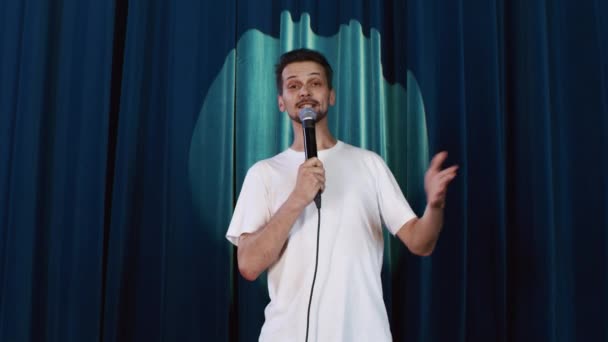 Comic man presenta un rendimiento stand-up en el escenario con micrófono contra cortina - Metraje, vídeo
