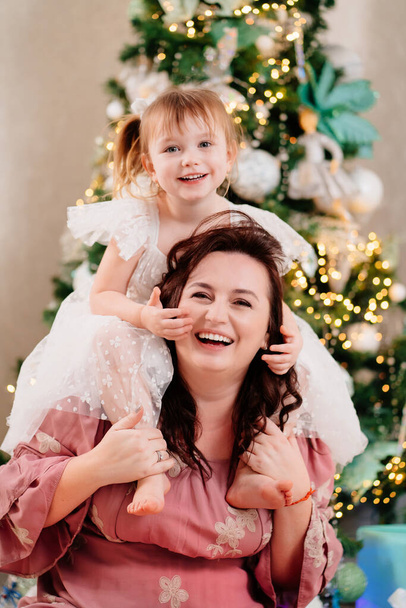 mom and daughter play at the Christmas tree.  - Foto, afbeelding