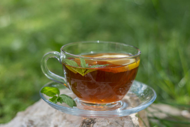庭の石の上に咲くお茶は、レモンと新鮮なミントの葉を添えています。選択的フォーカスガラス - 写真・画像
