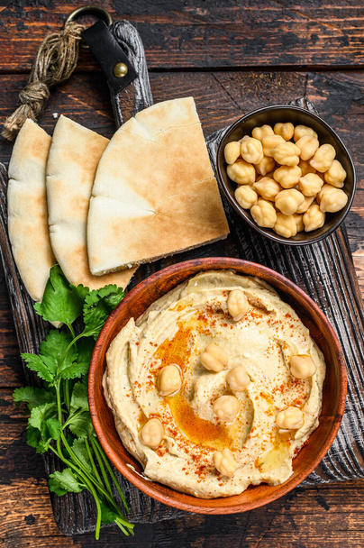 Hummus paste with pita bread, chickpea and parsley in a wooden bowl. Dark wooden background. Top view - Foto, afbeelding