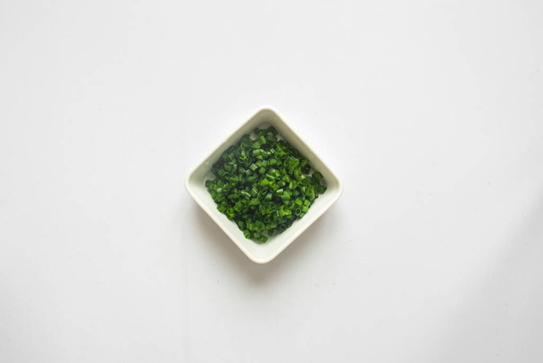 Κομμένα πράσινα κρεμμύδια σε λευκό πιάτο σε λευκό φόντο. πάνω όψη - Φωτογραφία, εικόνα