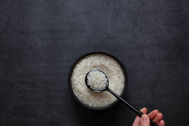 Rýže v misce a lžíce na tmavě šedém pozadí. - Fotografie, Obrázek