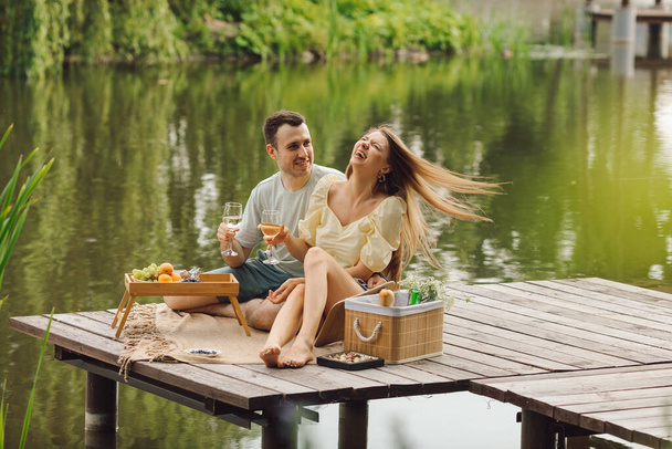 La pareja más feliz enamorada en el picnic en el día de verano en un hermoso lugar en el muelle de madera. Descanso y disfrute. Hermosos momentos de la vida. Super día. Relaciones románticas. Sensibilidad y cuidado.  - Foto, Imagen