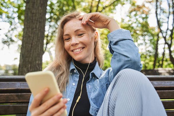 Happy girl looking at the smartphone and listening music at the park - Фото, изображение