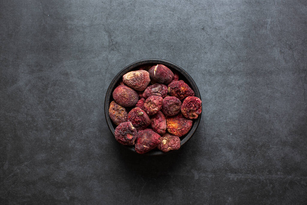 Der leuchtend rote Pilz ist ein gutes Nahrungsmittel Getrockneter roter Pilz in Schale auf dunkelgrauem Hintergrund. - Foto, Bild