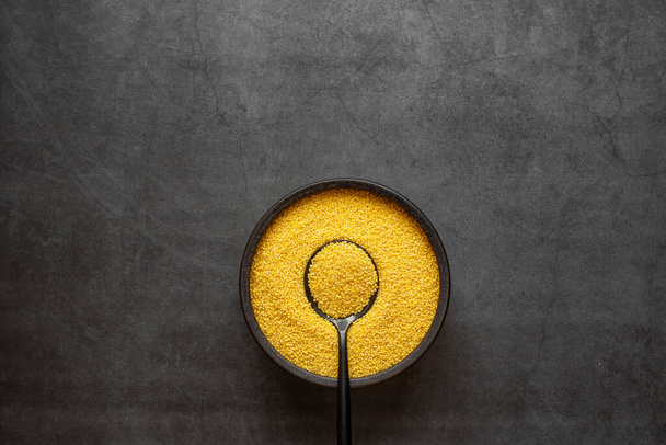 Yellow millet in spoon and bowl on dark grey background. - Фото, зображення