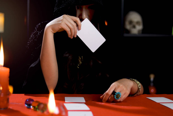 Bruja oscura en capucha negra sosteniendo tarjeta mágica, misterioso magnífico adivino hermosa mujer leer el futuro en la tarjeta, concepto de Halloween miedo. - Foto, imagen
