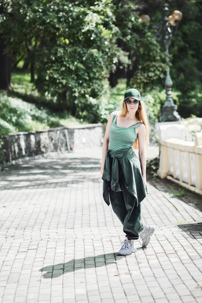 Zöld hip-hop ruhás lány sétál a sikátorban a parkban egy napos nyári napon. - Fotó, kép