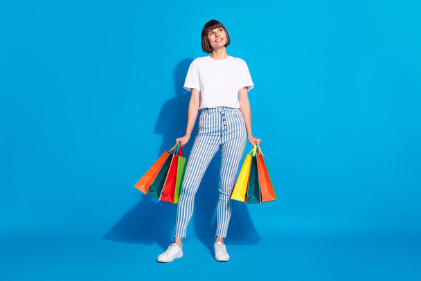 Tam boy vücut ölçülerinde fotoğrafçı kız, satıştan sonra çantaları tutuyor. Kopyalama alanı görünümlü, parlak mavi arkaplan - Fotoğraf, Görsel
