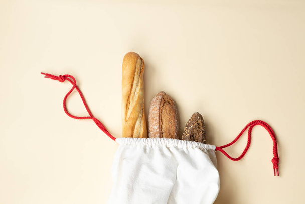 Verschiedene Brotsorten wie französisches Baguette, Roggen-Vollkornbrot und hefefreies Brot werden in einer wiederverwendbaren Baumwolltüte verpackt. Brot ist überall auf dem Kopf. Null-Abfall-Konzept.  - Foto, Bild