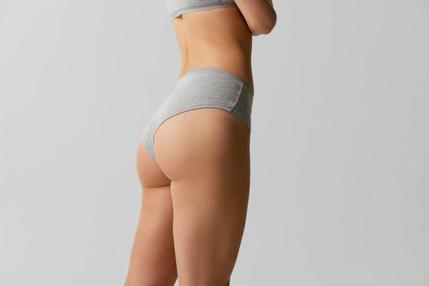 Vista posterior del cuerpo deportivo, nalgas de mujer joven en nalgas grises aisladas sobre fondo gris del estudio. Concepto de belleza natural - Foto, Imagen