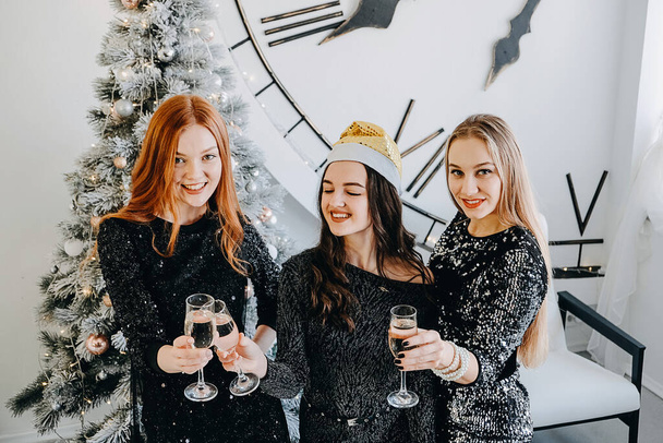 Празднование Рождества, новогодняя вечеринка, праздничные встречи друзей и вечеринки. Три красивые молодые женщины празднуют Новый год с небольшой группой друзей - Фото, изображение