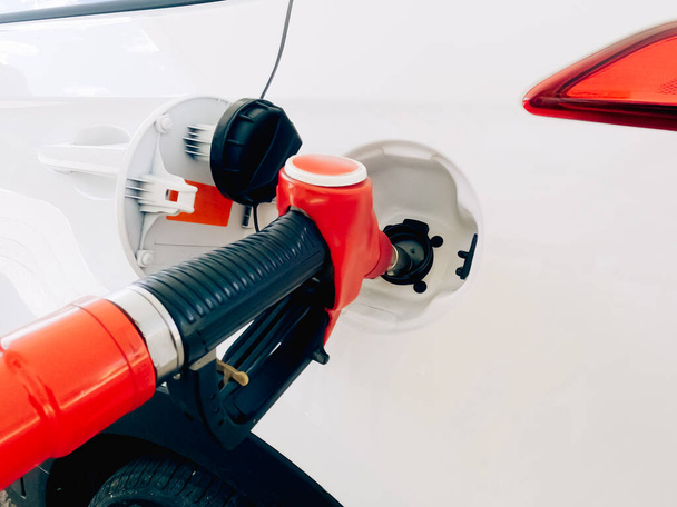 Ένα κόκκινο ακροφύσιο πλήρωσης εισάγεται στη δεξαμενή αερίου ενός λευκού αυτοκινήτου - Φωτογραφία, εικόνα