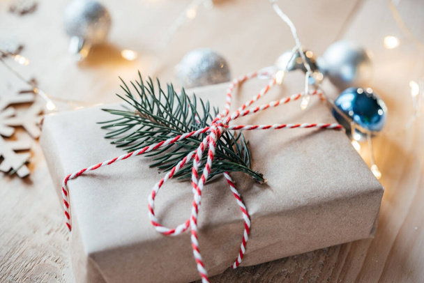 Χριστουγεννιάτικο κουτί δώρου τυλιγμένο σε χαρτί κραφτ με κλαδί πεύκου με χριστουγεννιάτικα φώτα και διακοσμήσεις - Φωτογραφία, εικόνα