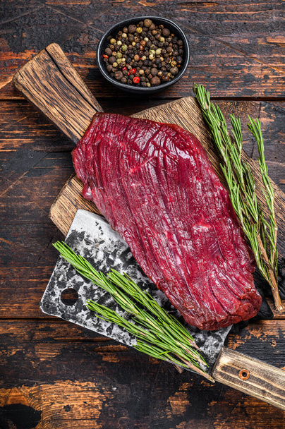 Venison raw meat steak on a cuuting board with rosemary. Black background. Top view - Photo, Image