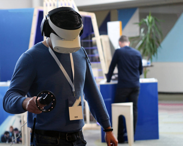 человек на выставке пробует виртуальную реальность в 3D очках, наушниках и дистанционном управлении - Фото, изображение
