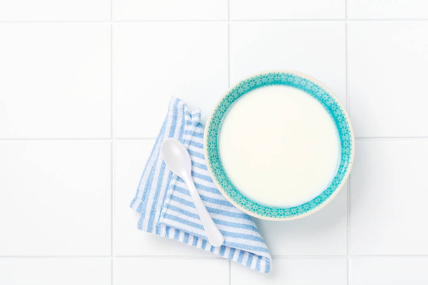 Greek yogurt in blue bowl, linen napkin and wooden spoon on white table. Top view - Фото, изображение