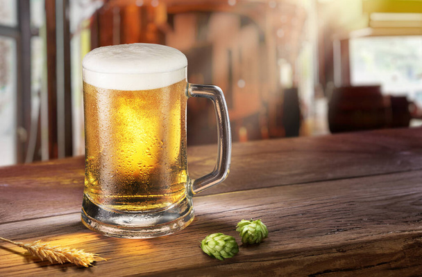 Cooled mug of pale beer with condensation drops on glass surface on the wooden table. Blurred bar at the background. - Photo, image