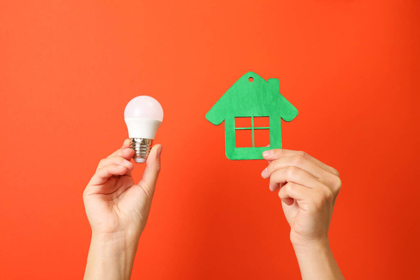 Mani tenere lampadina a risparmio energetico e la casa su sfondo rosso. - Foto, immagini